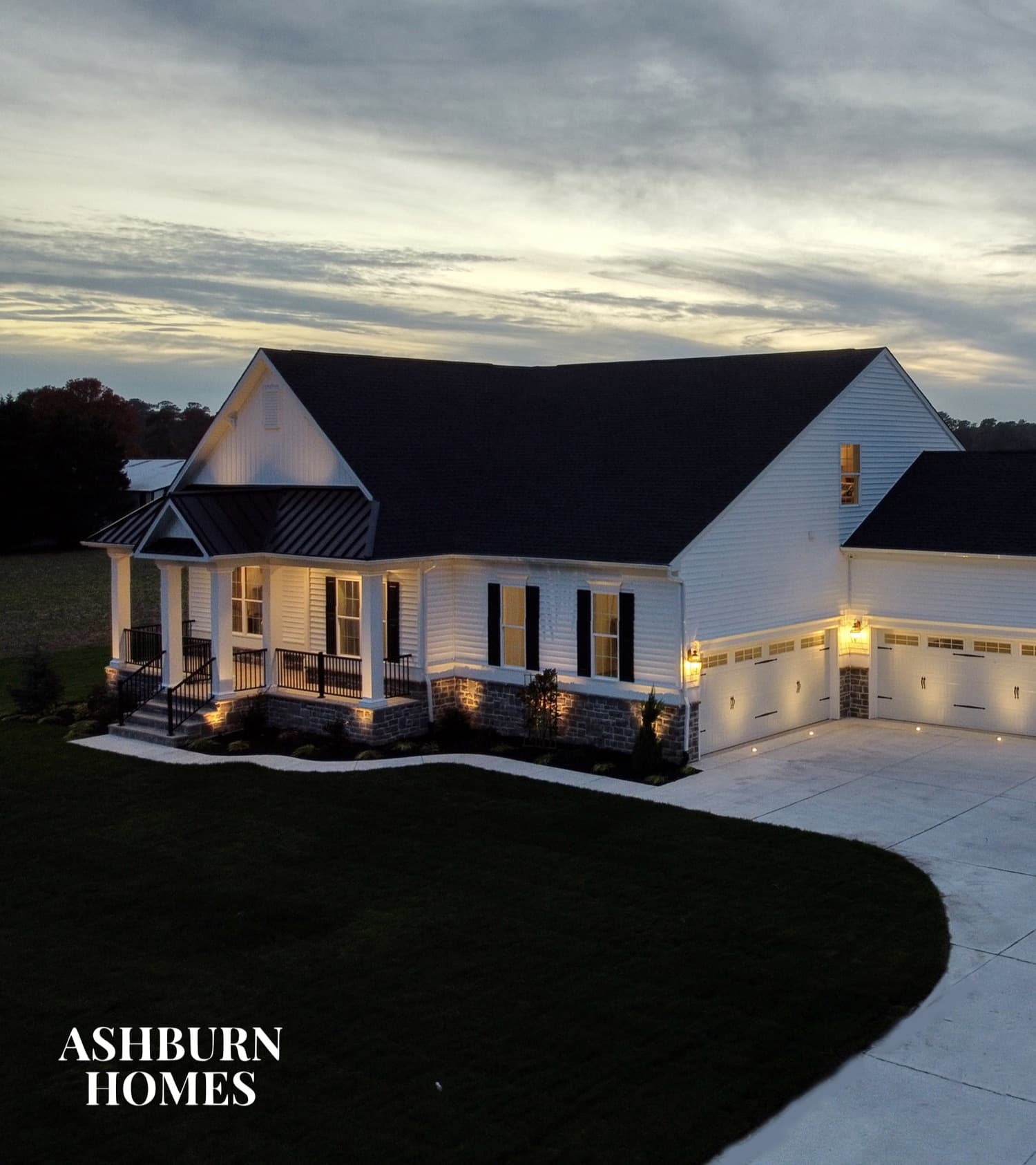 An Ashburn Homes house at dusk, lit from the porch and garage, with the Ashburn Homes logo.